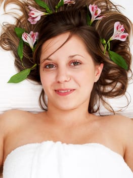 Young woman lying on white background with flowers in her hair waiting in spa studio for massage