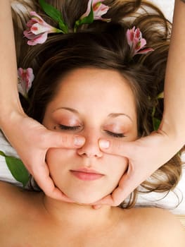 Young woman lying on white background with flowers in her hair waiting in spa studio for massage