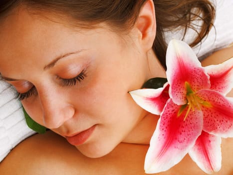 Young woman lying on white background with flowers in her hair waiting in spa studio for massage