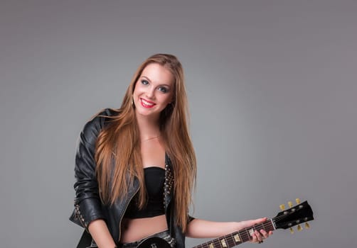 Beautiful girl  with long hair playing guitar in rock style on a gray background