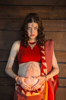Indian picture on woman hands and pregnant belly with henna tattoo on wooden wall background