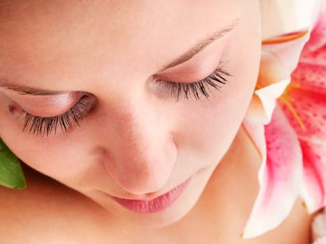 Young woman lying on white background with flowers in her hair waiting in spa studio for massage