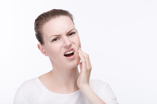 A young pretty woman in a white shirt holds her cheek from toothache