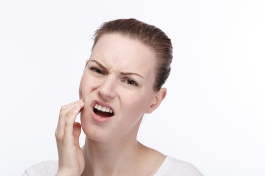 A young pretty woman in a white shirt holds her cheek from toothache