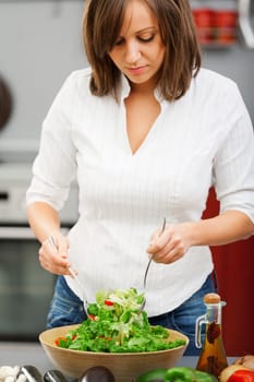 Young woman making salad in the kitchen and pooring olive oil