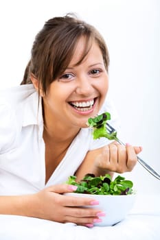 Young woman eating healthy salad isolated on white background lying on the bed
