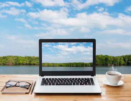 laptop computer and coffee on wood workspace and mangrove forest background