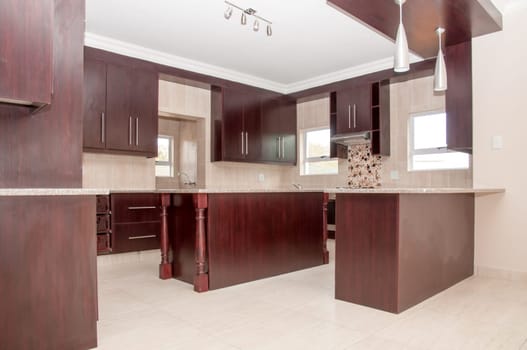 A Brand nwe kitchen of dark wood and granite tops installed in a newly build house with tiled floors.