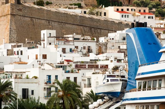 The funnel of a luxury yacht and a tender boat are in view in front of the old town of Ibiza island in the Medeteranean.