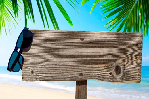 Empty wooden sign with sunglasses on the beach
