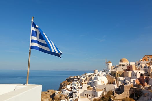 White villa houses and hotels with a perfect view of the volcano in the sea, Oia, Santorini Greek flag in front