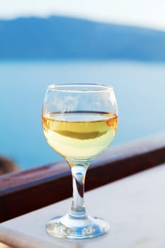 A single glass of white wine on a table in a summer resort with a perfect view to the volcano