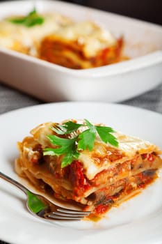 Typical italian lasagna served in a plate, one portion in front, baking dish blurred in the background