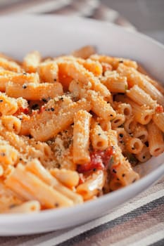 Penne with tomatos and parmesan cheese served in a white plate, close up