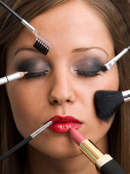 Close up of young woman face with all kinds of make up tools - brush, lipstick etc.