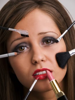 Close up of young woman face with all kinds of make up tools - brush, lipstick etc looking very bored or sad