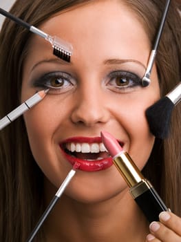 Close up of young woman face with all kinds of make up tools - brush, lipstick etc.