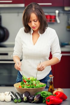 Young woman making salad in the kitchen and pooring olive oil