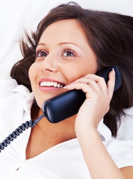 Young woman lying in bed and talking on the phone isolated on white background