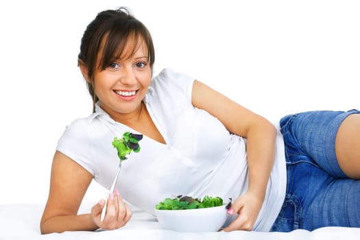 Young woman eating healthy salad isolated on white background lying on the bed