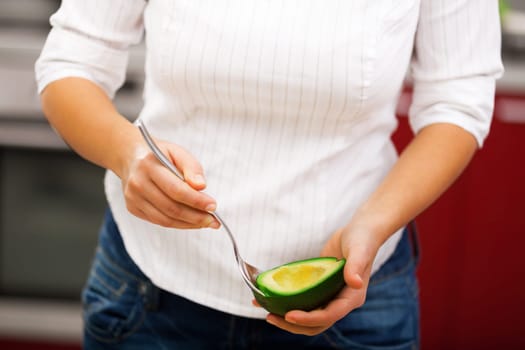 Young woman making salad in the kitchen - peeling avocado