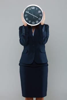 Businesswoman holdng a clock in front of her face isolated on gray background