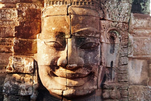 Dramatic view at sunset of one of the many large stone carved faces of Bayon Temple in Angkor Thom, Angkor district, Siem Reap, Cambodia