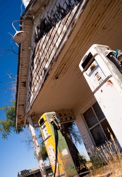 Two broken down and rusted gas pumps stand out front of a broken down building