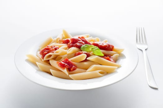 Plate of penne pasta with tomato sauce and basil close up.