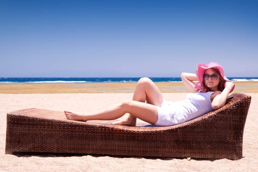 Young woman in a hat relaxes on a lounger on the beach.