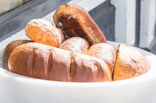 Rustic breads made of wheat in a white basket in front of a bakery.