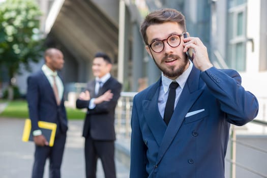Portrait of multi ethnic business team.Three men standing against the background of city. The foreground of a European man  talking on the phone. Other men is Chinese and African-American.