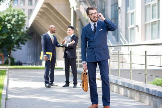 Portrait of multi ethnic business team.Three men standing against the background of city. The foreground of a European man  talking on the phone. Other men is Chinese and African-American.