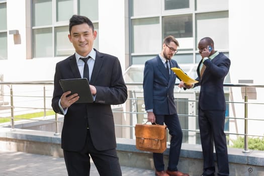 Portrait of multi ethnic business team. Three happy smiling men standing against the backdrop of the city.  The foreground of a Chinese  man  with laptop