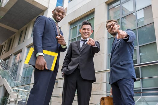 Close-up of multi ethnic business team holding their thumbs up. Three  men pointing into the camera against the backdrop of the city. The one man is European, other is Chinese and African-American.