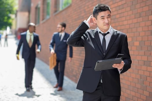 Portrait of multi ethnic business team. Three happy smiling men standing against the backdrop of the city.  The foreground of a Chinese  man  with phone and laptop