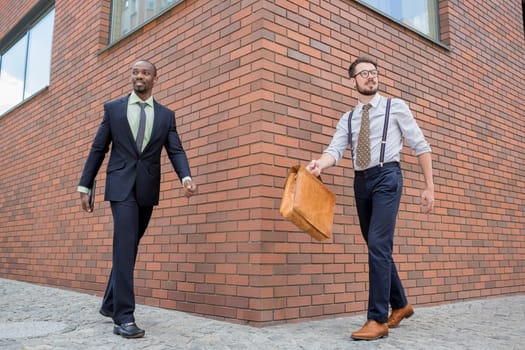 Portrait of multi ethnic business team. Two happy smiling men  walking against the backdrop of the city. The one man is African-American, other is European.