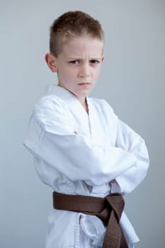 Young boy in karate clothing, posing with a tough expression on his face and his arms folded.