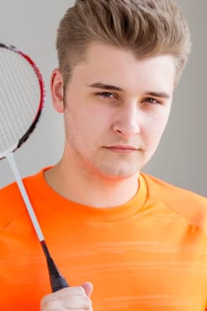 Portrait of a teenage boy. He is holding a badminton racket and standing against a plain background