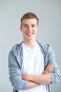 Portrait of a young man on a white background. His arms are folded and he is smiling for the camera.