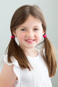 Portrait of a young girl. She has her hair in pigtails and is smiling at the camera against a plain blackground