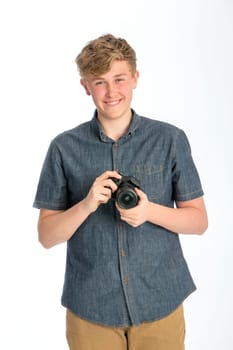 Teenage boy posing with a camera in his hands. He is standing against a white background and smiling for the camera.