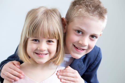 Young boy and girl dressed up formally and posing for the camera together on a white background