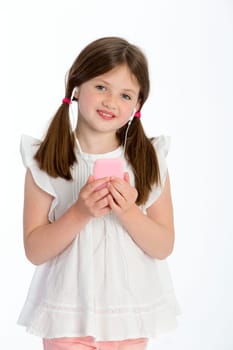 Little girl listening to music through headphones on a smartphone. She is smiling at the camera and standing against a white background.