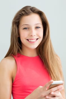 Portrait of a teenage girl using a smartphone. She is smiling at the camera against a plain background.
