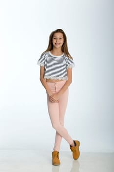 Full length portrait of a young girl against a white background. She is smiling for the camera.