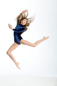 Gymnast posing in mid air against a white background. She is wearing a blue leotard.