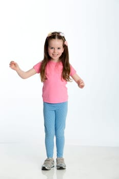 Young girl posing for the camera with her arms out. She is standing against a white background and is smiling at the camera.