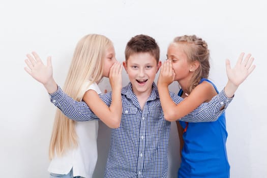 Teenage girls whispering in the ears of a secret teen boy on white background