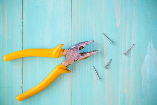 Yellow pliers and few nails on wood background